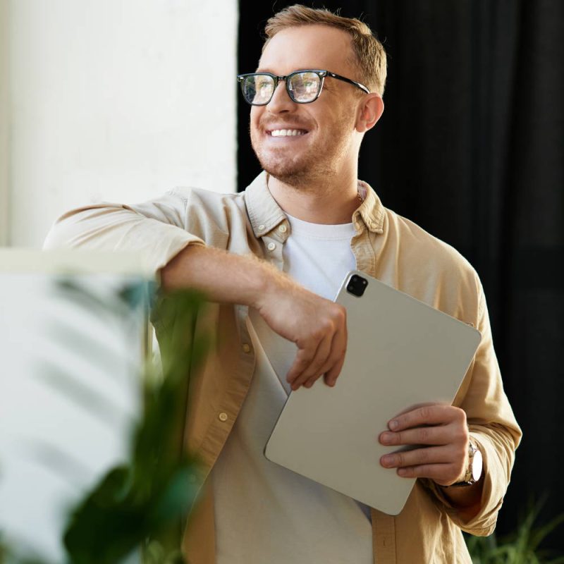 man holding laptop standing by a plant